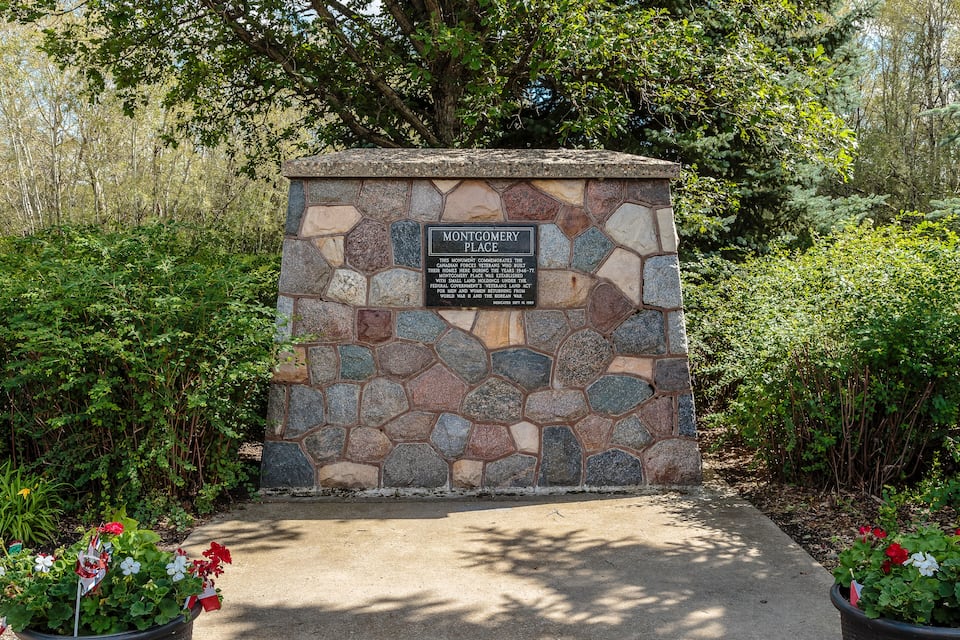 A stone monument with a plaque reading "Montgomery Place" surrounded by greenery and flowers.