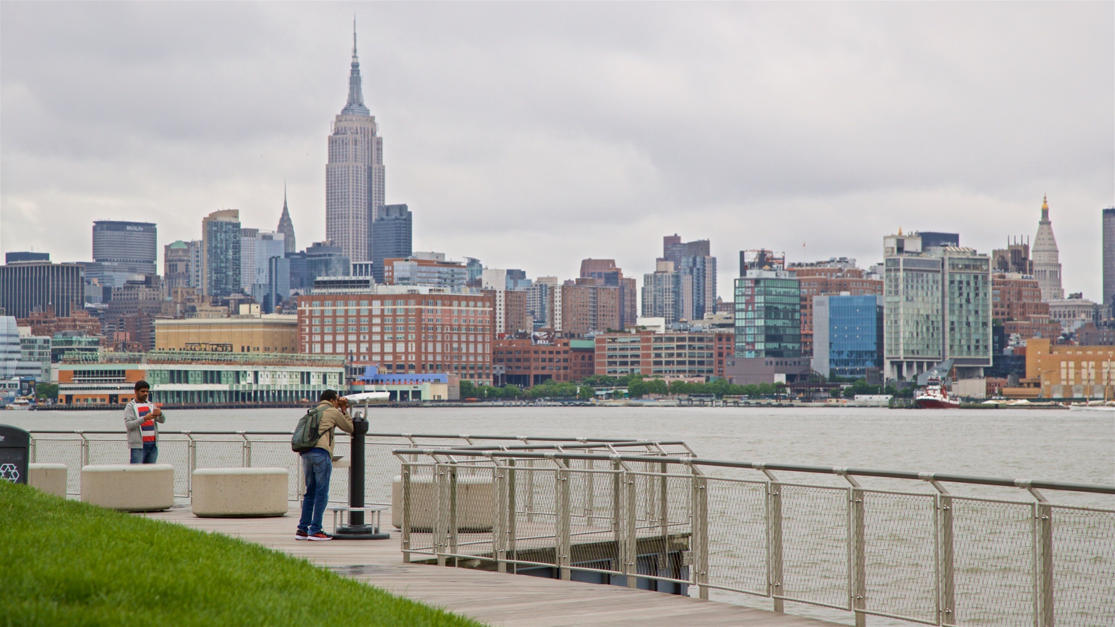 A waterfront promenade with a city skyline in the background, including the Empire State Building.