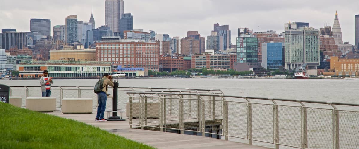 A waterfront promenade with a city skyline in the background, including the Empire State Building.