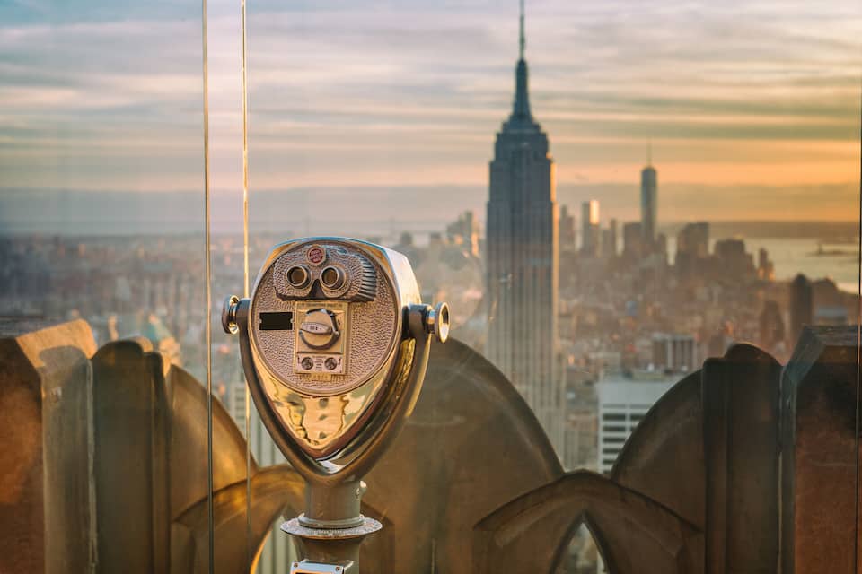 A vintage telescope with a cityscape in the background, including a prominent skyscraper.