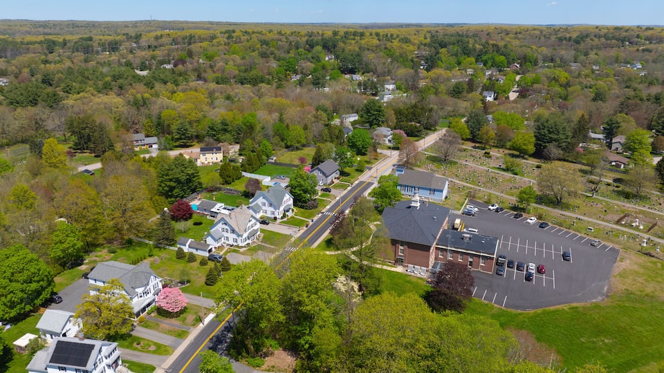 An aerial view of a suburban neighborhood with houses, a cemetery, and a parking lot.