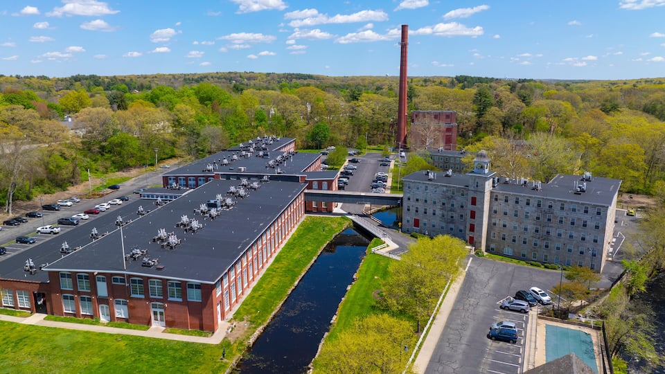 An industrial complex with a tall chimney, a river, and a parking lot.