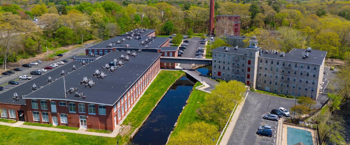 An industrial complex with a tall chimney, a river, and a parking lot.