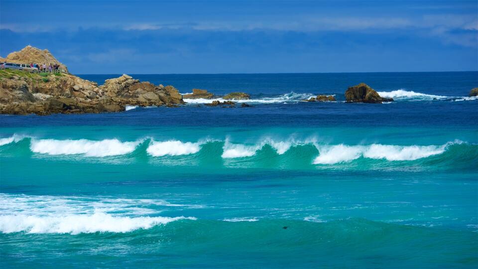 A rocky coastline with waves crashing against the shore and a group of people on a cliff.