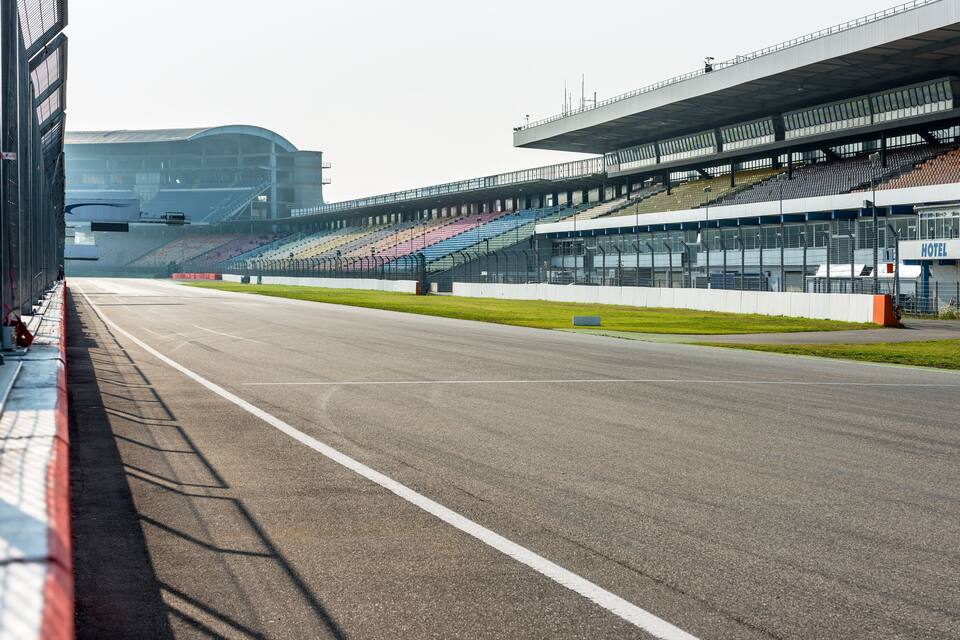 Uma pista de corrida com arquibancadas vazias e um hotel ao fundo.