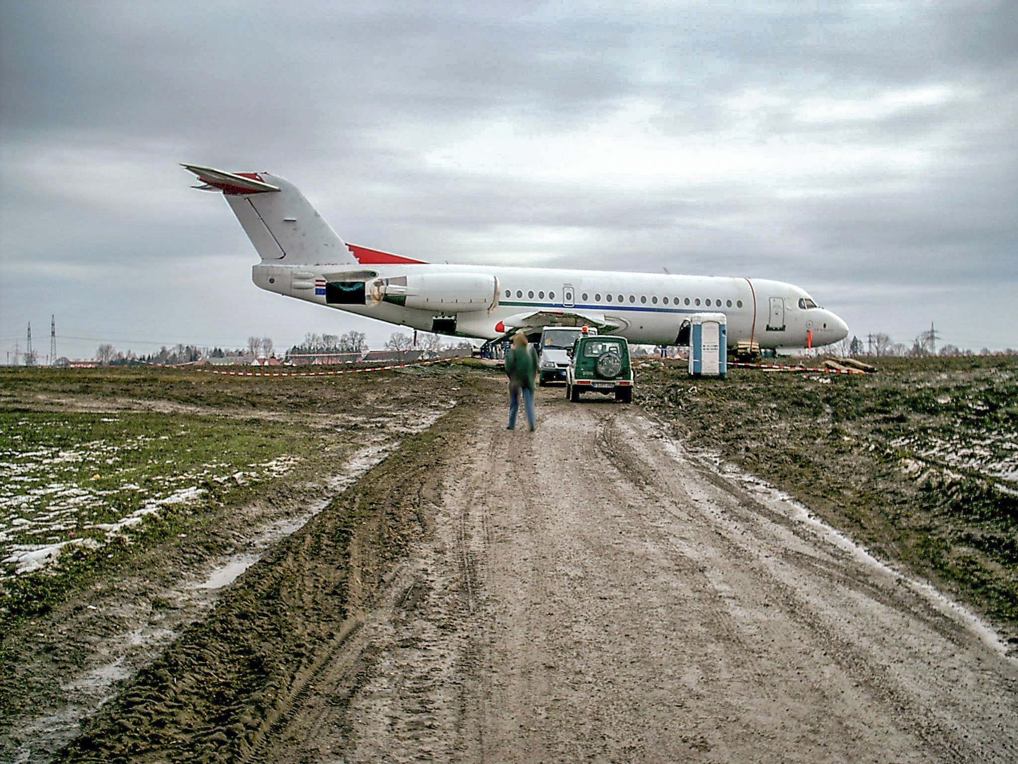 A large white airplane with red accents parked on a muddy road.