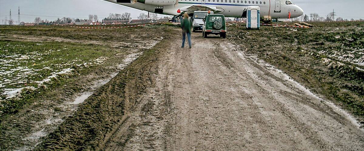 A large white airplane with red accents parked on a muddy road.