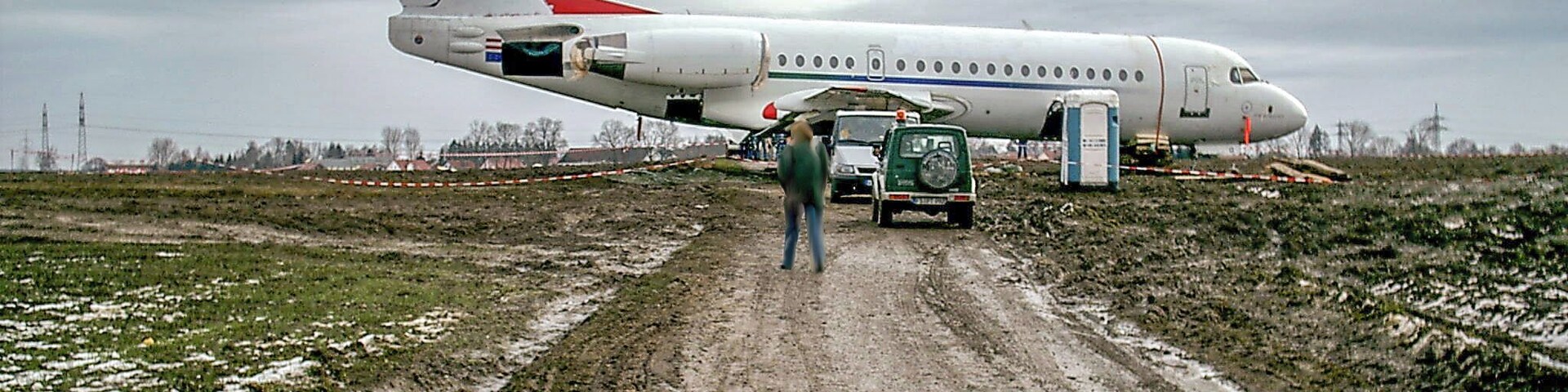 A large white airplane with red accents parked on a muddy road.