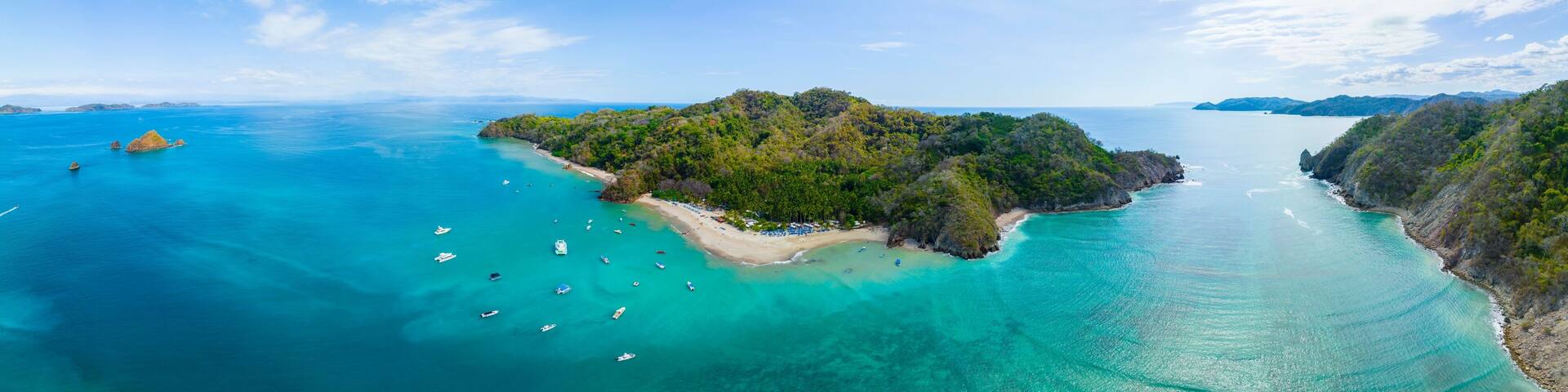 A tropical island with clear turquoise waters, surrounded by lush greenery and rocky outcrops.