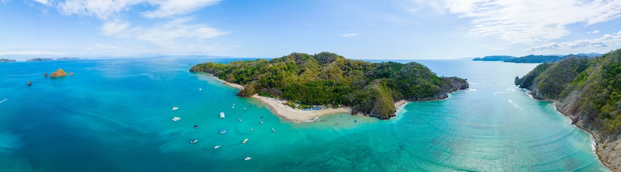 A tropical island with clear turquoise waters, surrounded by lush greenery and rocky outcrops.