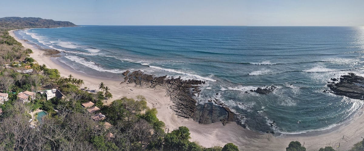 A coastal landscape with a beach, rocky shoreline, and residential buildings.