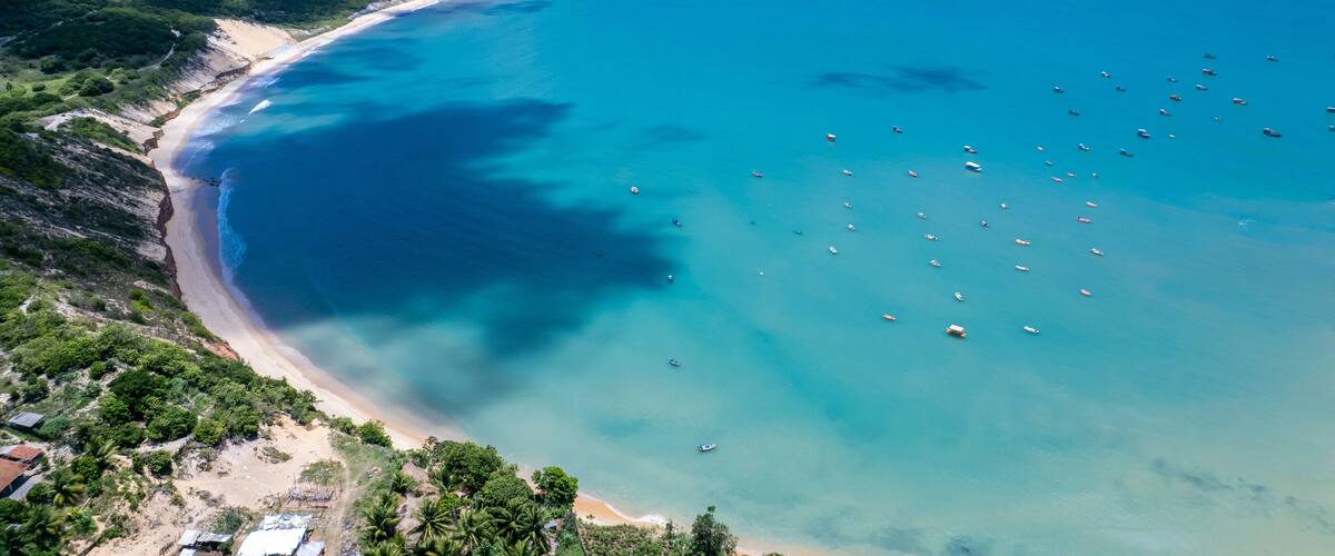 Un paysage côtier avec une plage de sable, des eaux turquoise et limpides, et quelques bateaux dispersés.