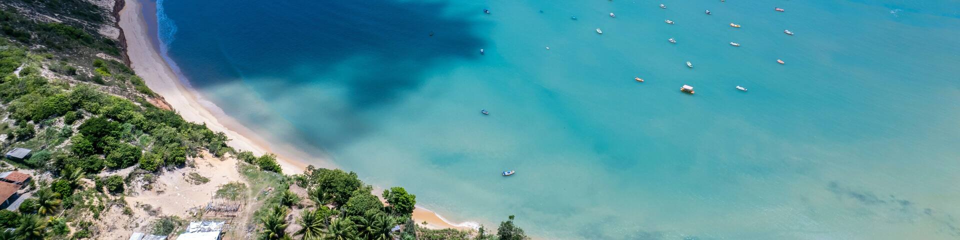 A coastal landscape with a sandy beach, clear turquoise waters, and scattered boats.