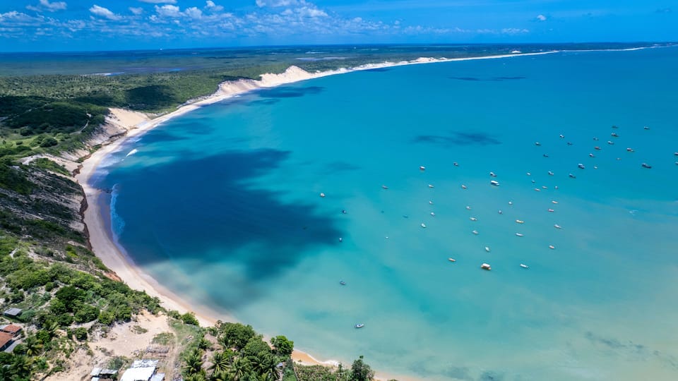 A coastal landscape with a sandy beach, clear turquoise waters, and scattered boats.