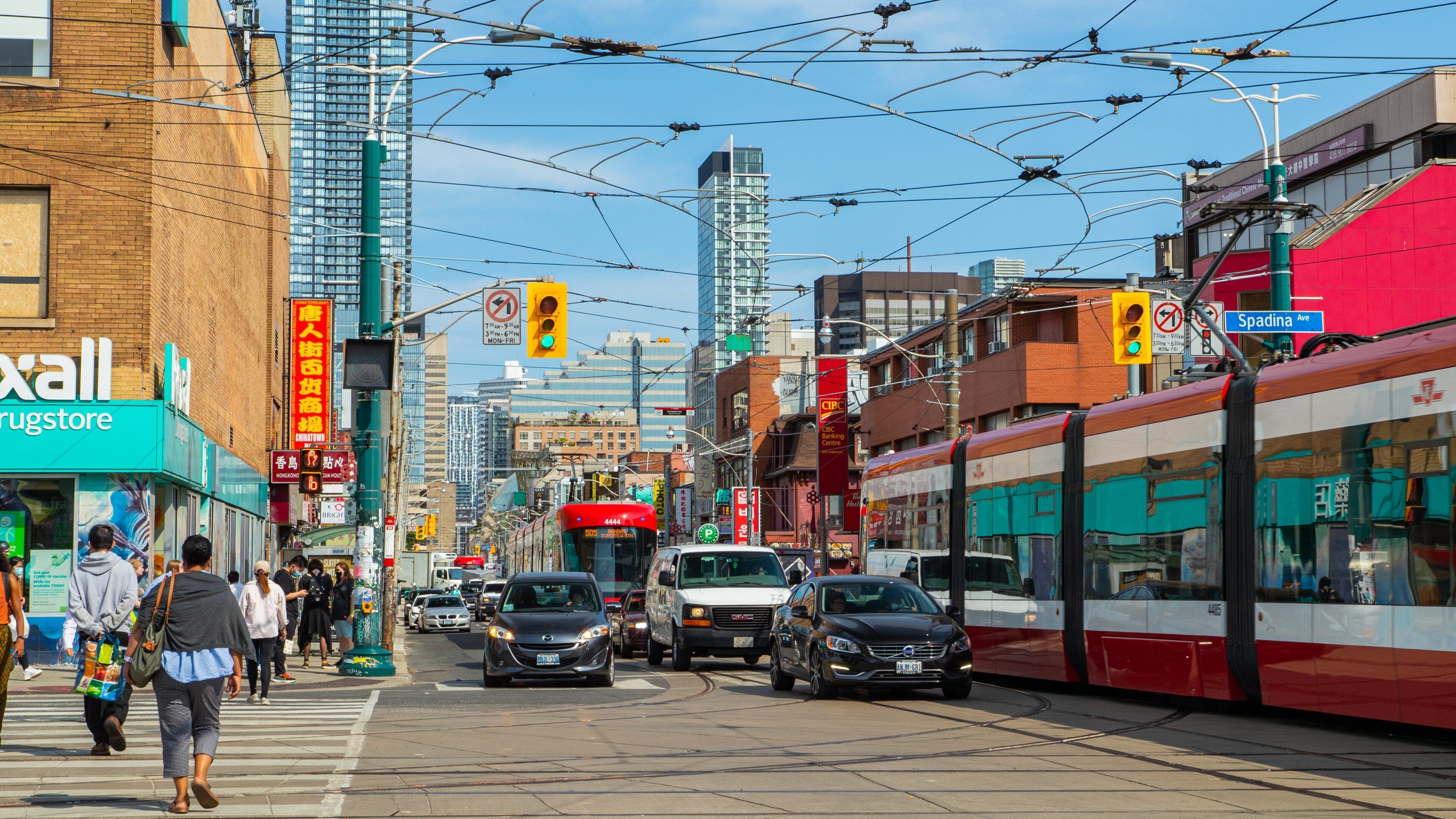 A busy urban street with tram tracks, cars, and pedestrians.