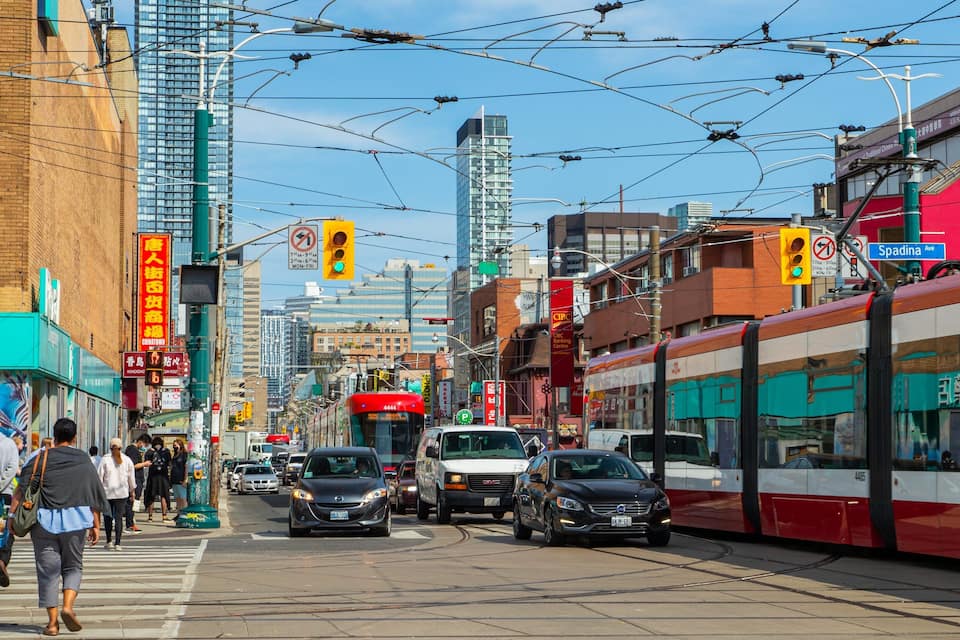 A busy urban street with tram tracks, cars, and pedestrians.