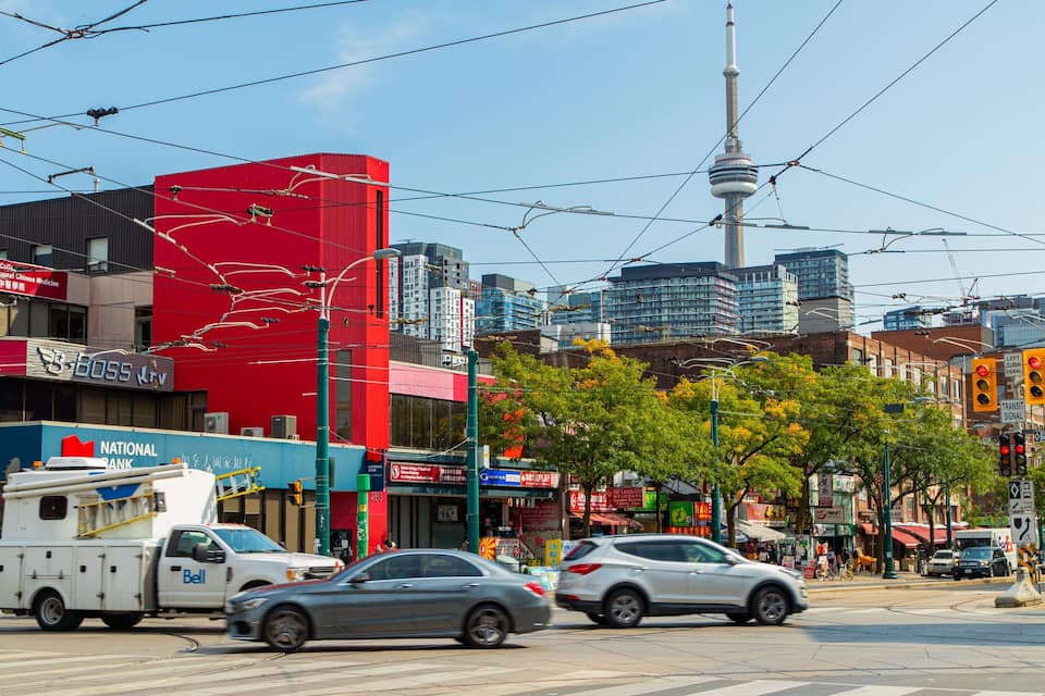 A busy urban street with tram tracks, a red building, and a tower in the background.