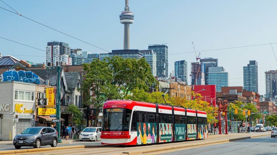 Un autobus rouge, arborant les inscriptions publicitaires « Service public » et « Service mobile » sur ses flancs, circule dans une rue de la ville, avec des immeubles et une tour en arrière-plan.