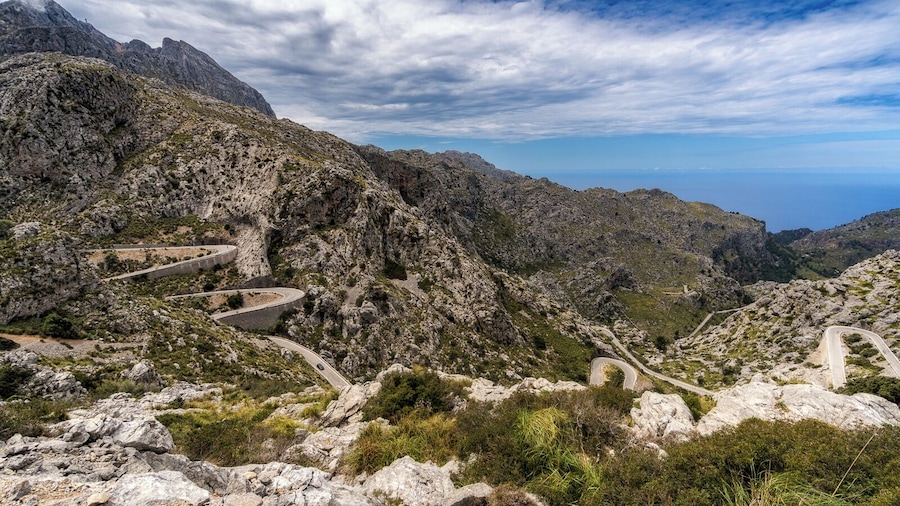 A winding mountain road with rocky terrain and sparse vegetation.