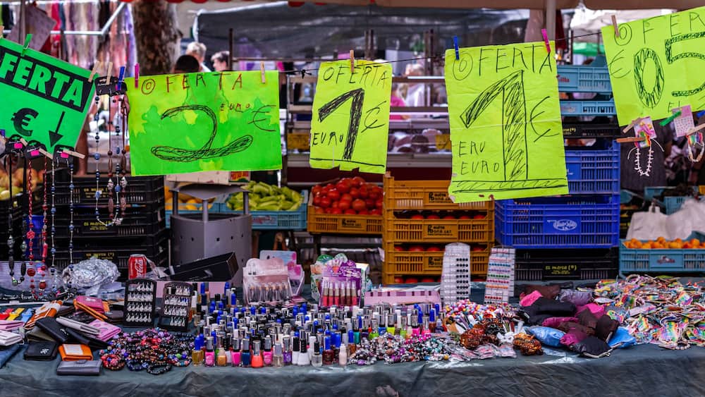 A market stall with various items for sale, including jewelry, cosmetics, and fruits.