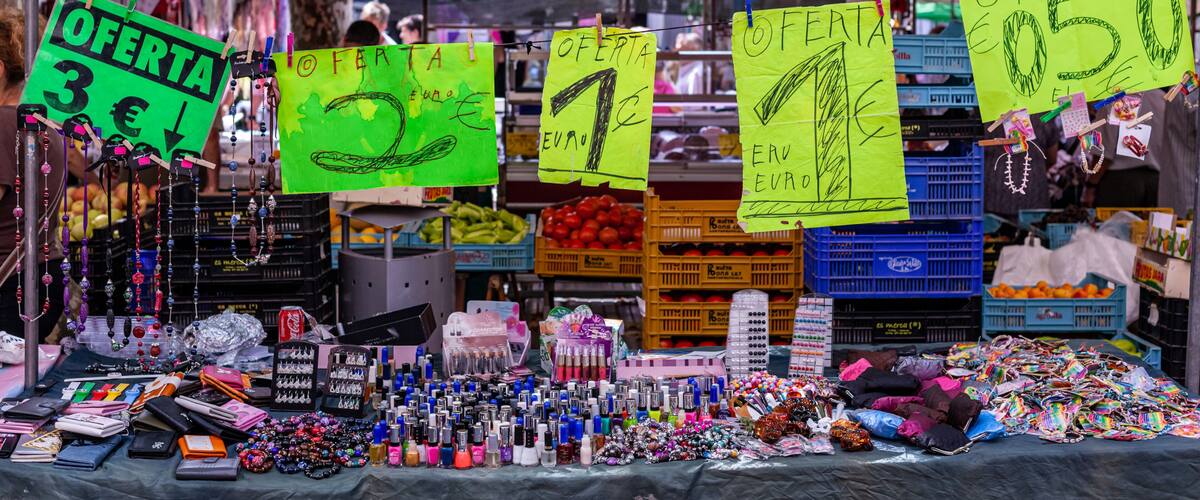 A market stall with various items for sale, including jewelry, cosmetics, and fruits.