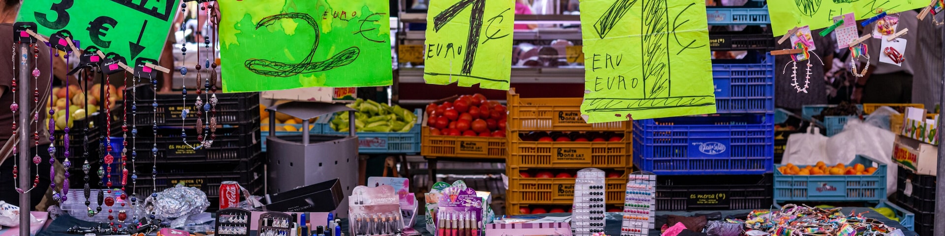 A market stall with various items for sale, including jewelry, cosmetics, and fruits.