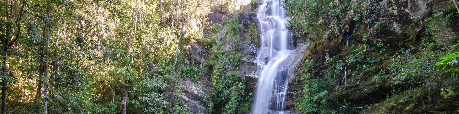 A waterfall cascading into a clear turquoise pool surrounded by rocky terrain and dense green foliage.