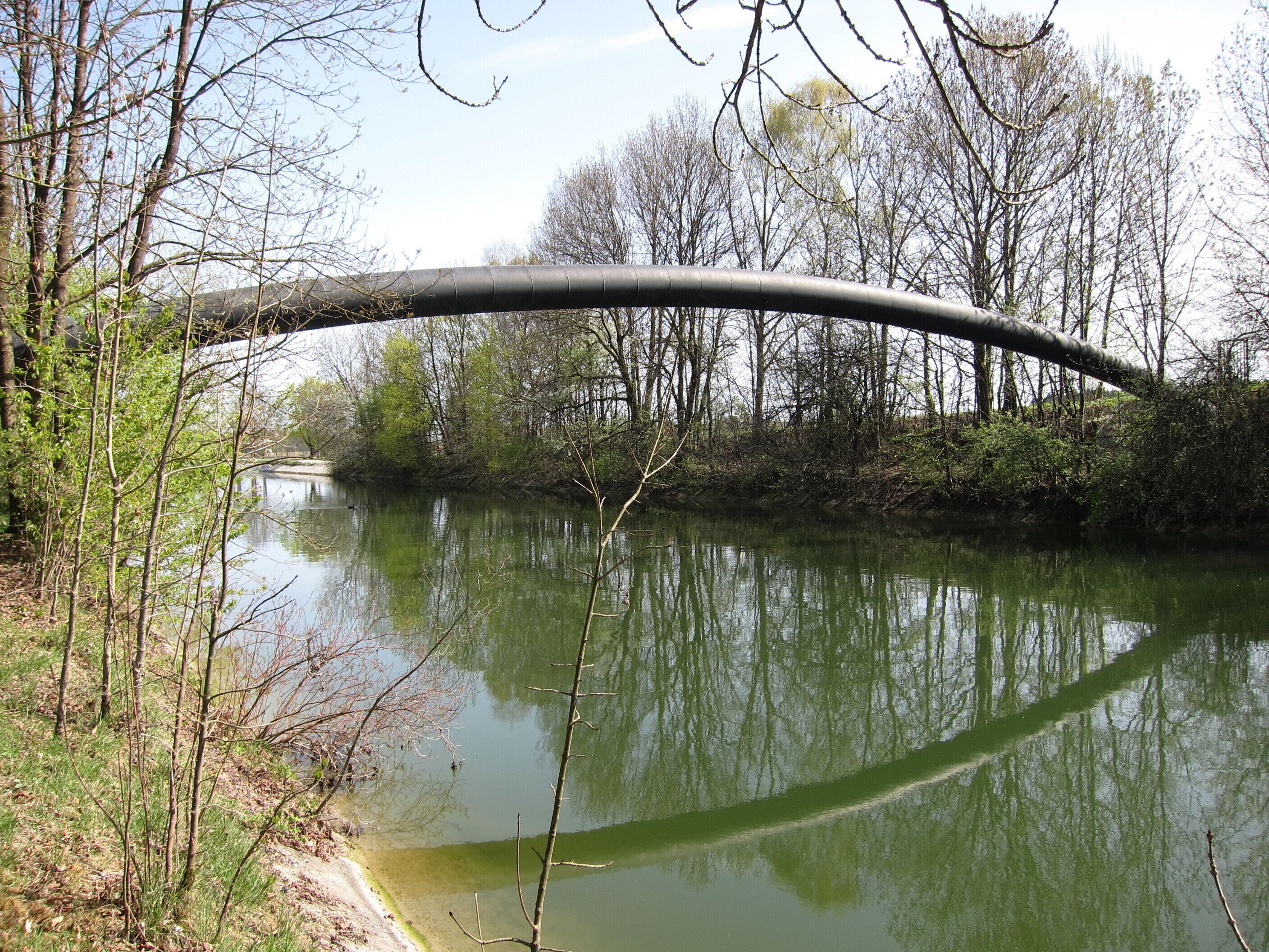 A river with a curved bridge, surrounded by trees and greenery.