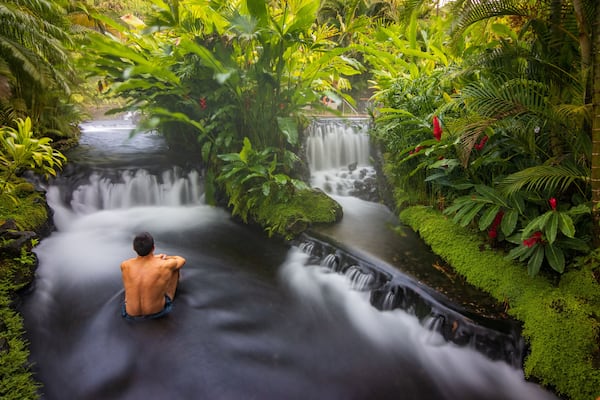 Une cascade au cœur d’une forêt verdoyante, avec une personne assise à son pied.
