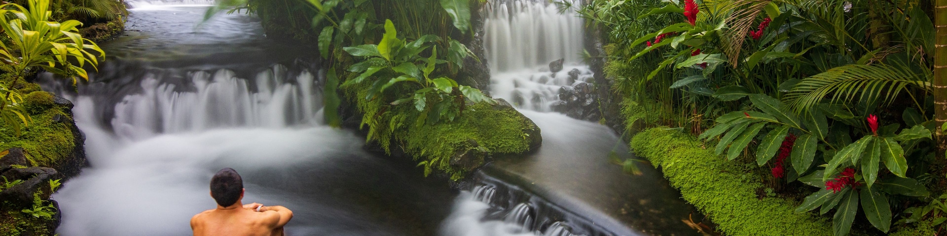 Une cascade au cœur d’une forêt verdoyante, avec une personne assise à son pied.