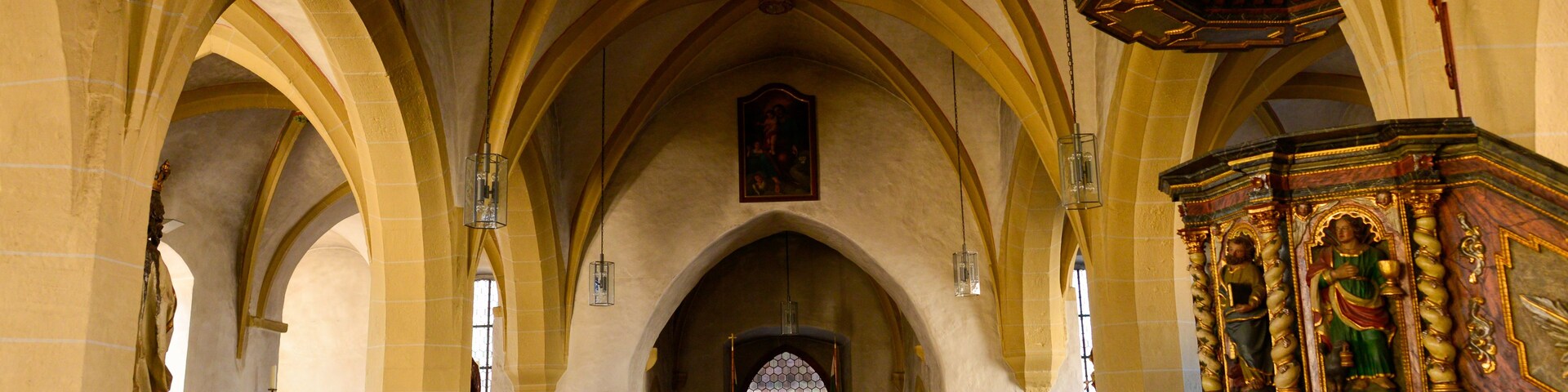 Interior de una iglesia con techos abovedados, bancos de madera y un altar decorativo.