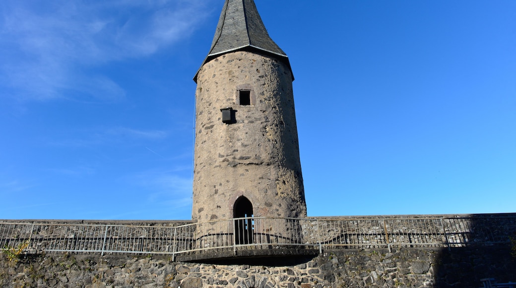 Ein hoher, zylindrischer SteinTurm mit einem spitzen Dach, einem kleinen Fenster und einer Tür, umgeben von einer Steinmauer und einem MetallGeländer.