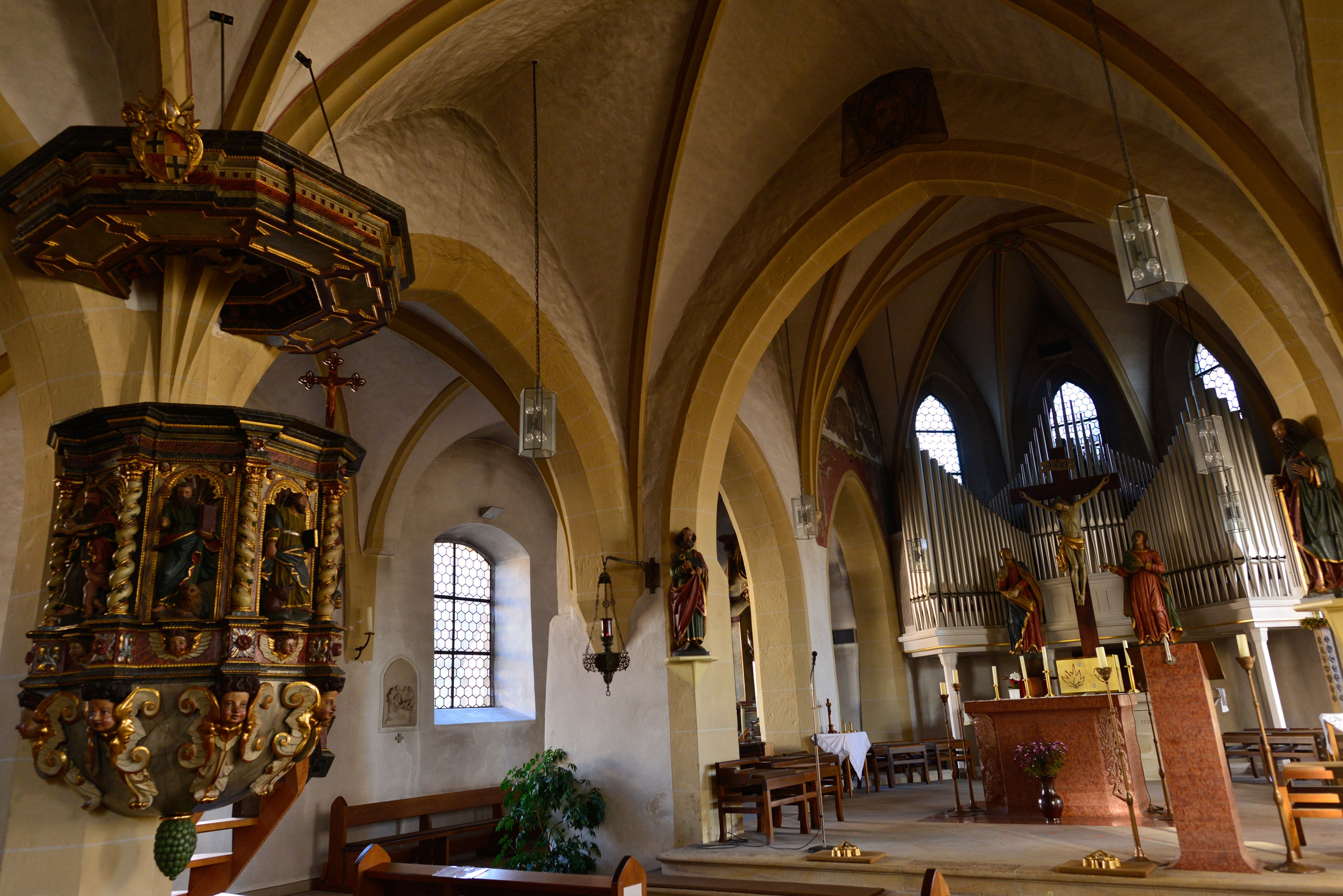 Innenansicht einer Kirche mit gewölbter Decke, einer Holzbühne und einer Orgel.