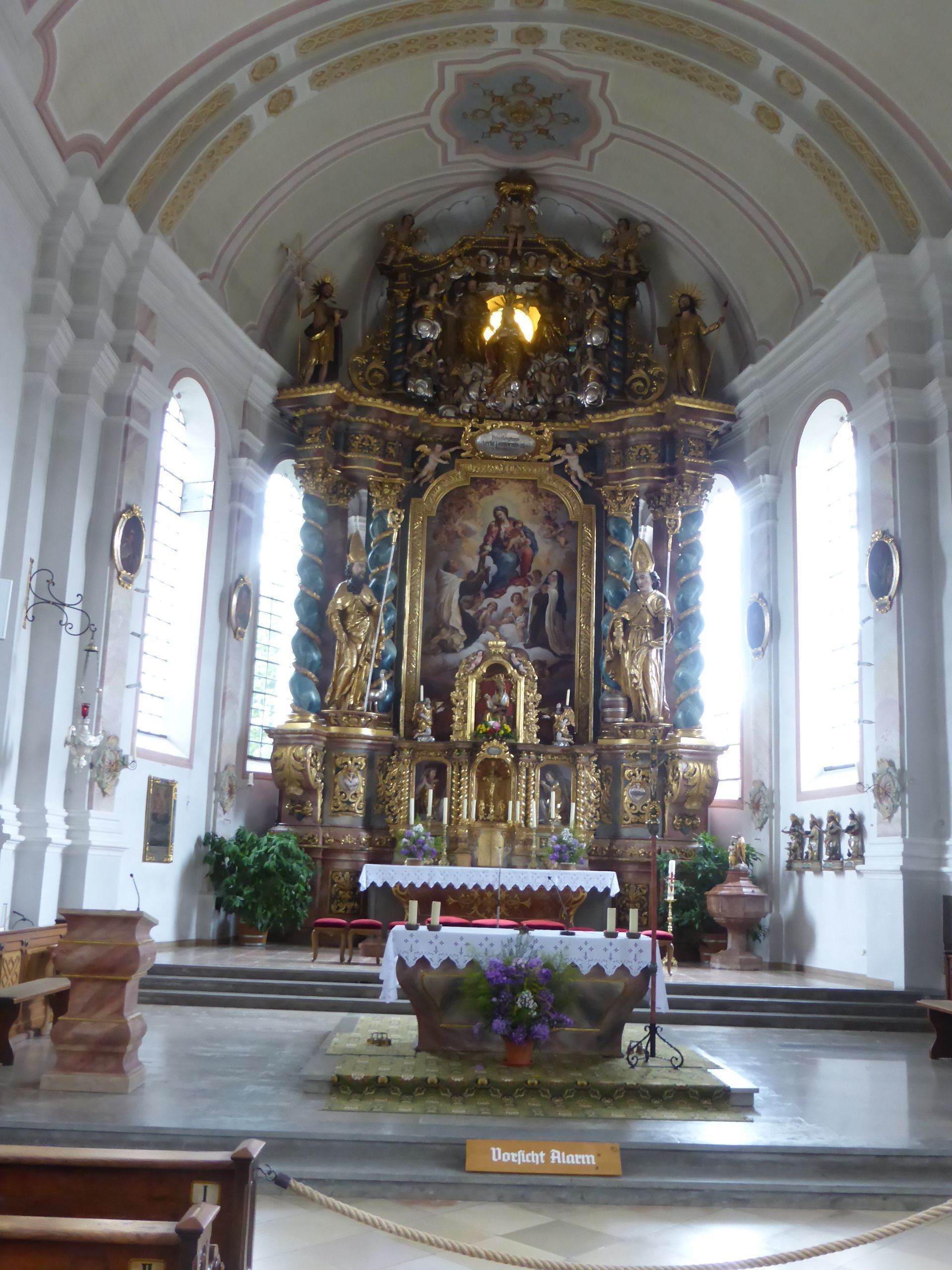An ornate church interior with a central altar, statues, and a large mural.