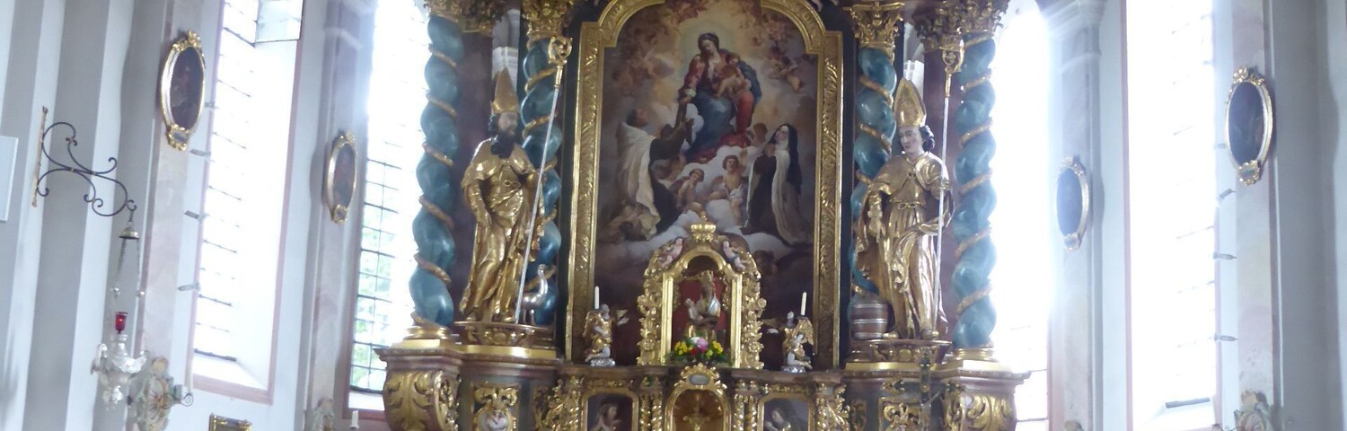 An ornate church interior with a central altar, statues, and a large mural.