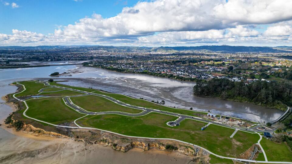 An aerial view of a coastal area with a river, green park, and a city in the background.