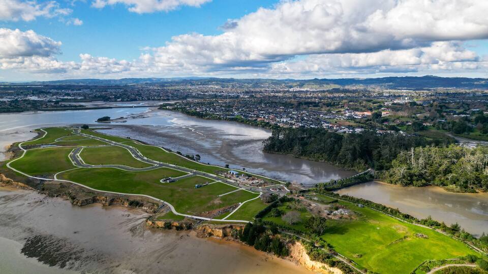 An aerial view of a coastal area with a river, green fields, and a town in the background.