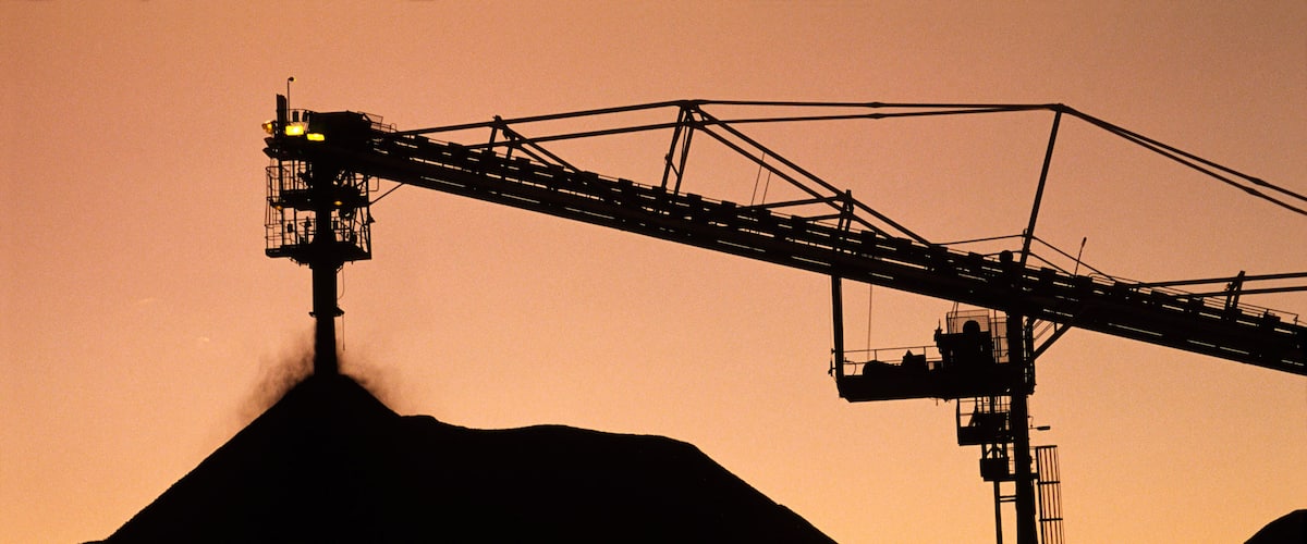 A silhouette of a mining operation with a large crane and a hill.