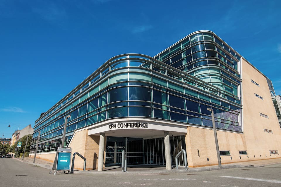 Een modern gebouw met een gebogen glazen gevel en een bord waarop “OPH CONFERENCE” staat.