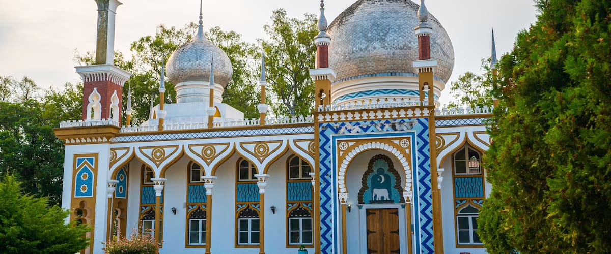 A mosque with two domes, a minaret, and intricate blue and gold patterns.