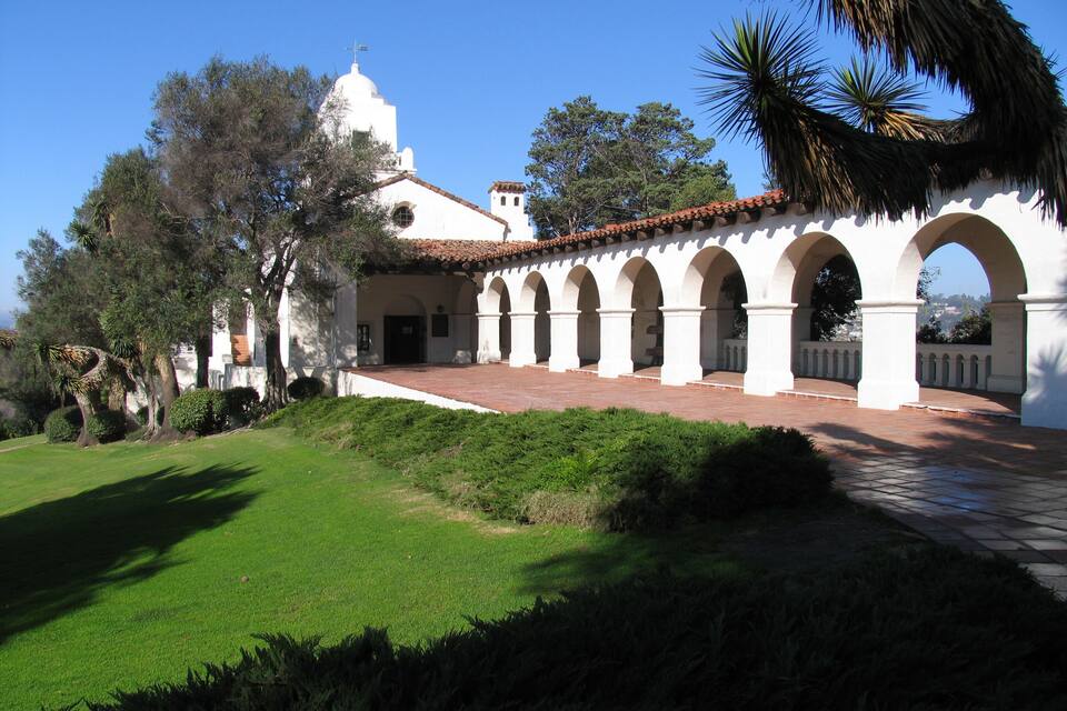 A white building with a red-tiled roof, white arches, and a dome.