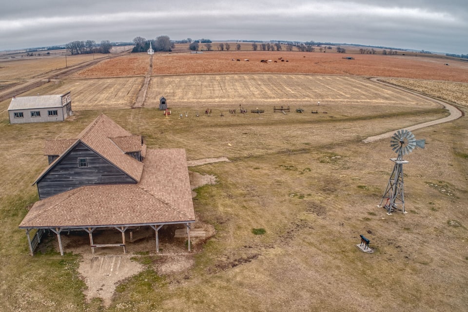 A rural landscape with a windmill, a barn, and a field of cows.