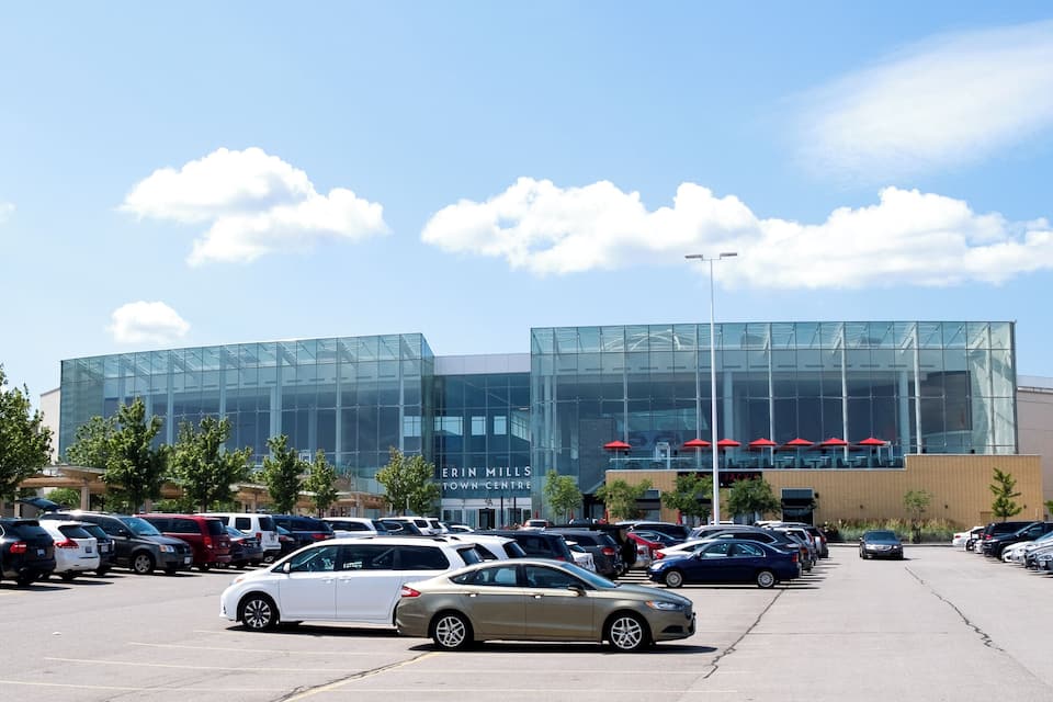 Un parcheggio di fronte a un edificio moderno con finestre in vetro e un cartello che riporta la scritta 'ERIN MILLS TOWN CENTRE'.