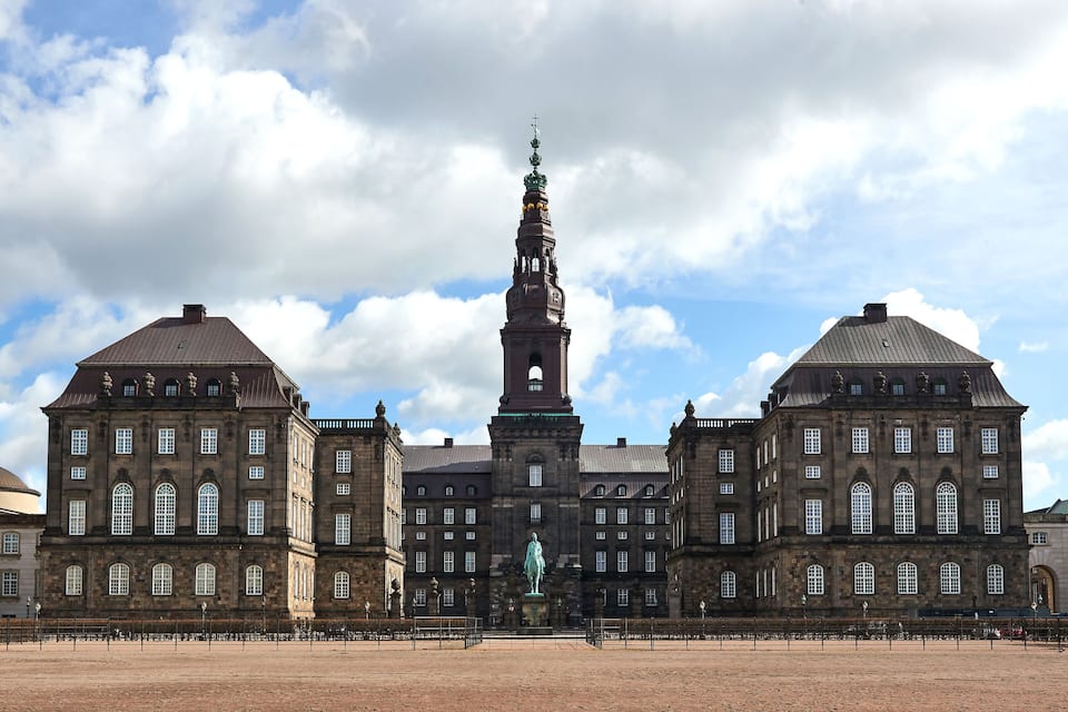 A historic building with a central tower and statue, surrounded by a plaza.