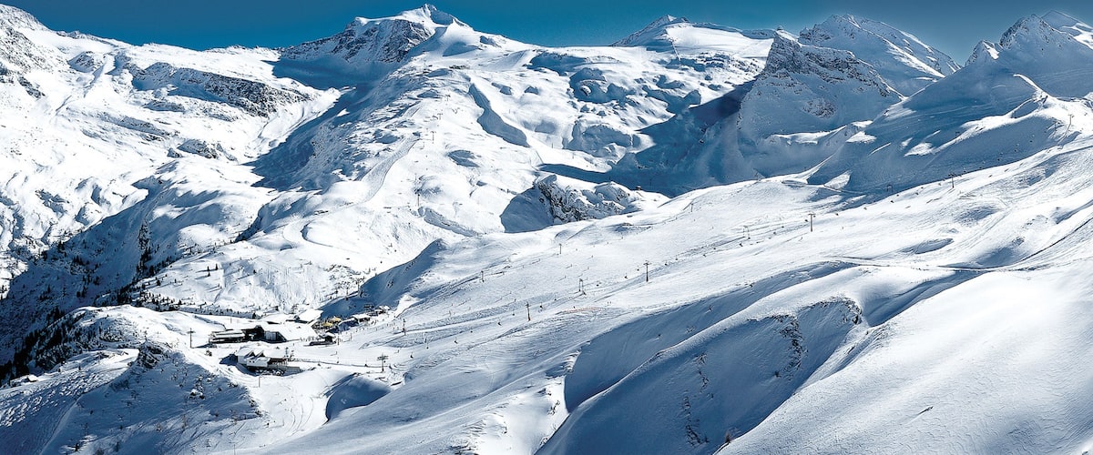 A snow-covered mountain range with ski slopes and a clear blue sky.