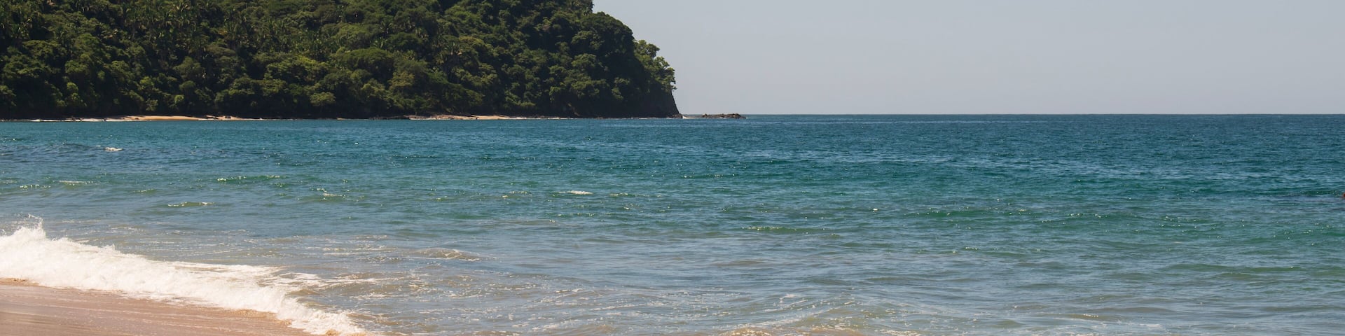 Beautiful landscape of a beach in the mexican pacific coast in a sunny day with a blue and clear sky, trees, palms and green hills, some waves and sand in the beach