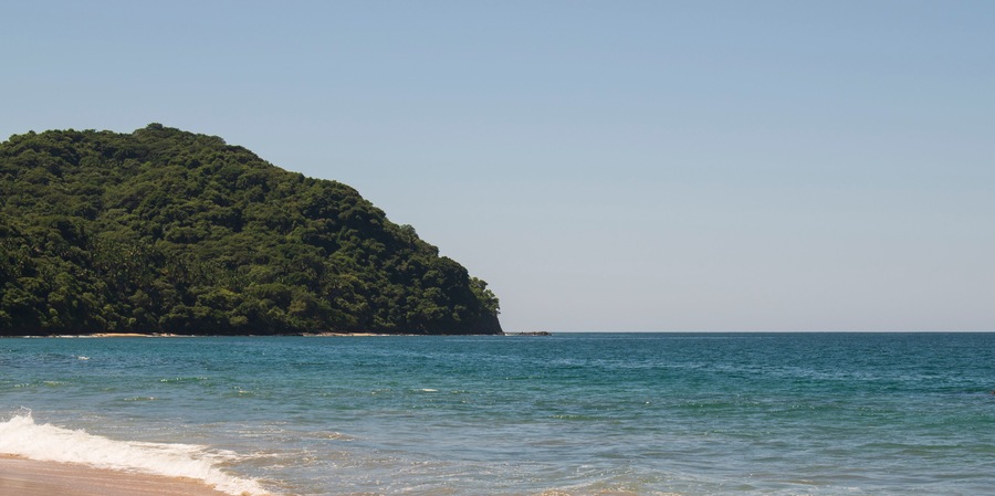 Beautiful landscape of a beach in the mexican pacific coast in a sunny day with a blue and clear sky, trees, palms and green hills, some waves and sand in the beach