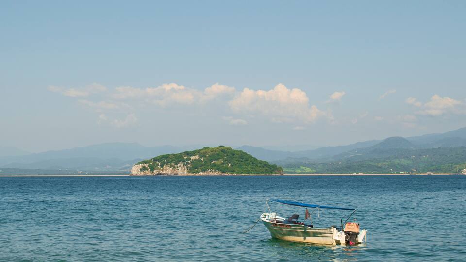 A fishing boat in a mexican beach of the pacific coast with and island behind in a sunny day with a clear blue sky and some mountains in the background