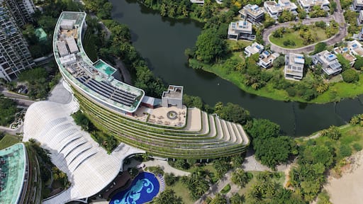 Aerial view of Forest City featuring modern curved architecture with green terraces, a swimming pool, and surrounding lush landscape by the water in Gelang Patah, Johor Darul Ta'zim, Malaysia.
