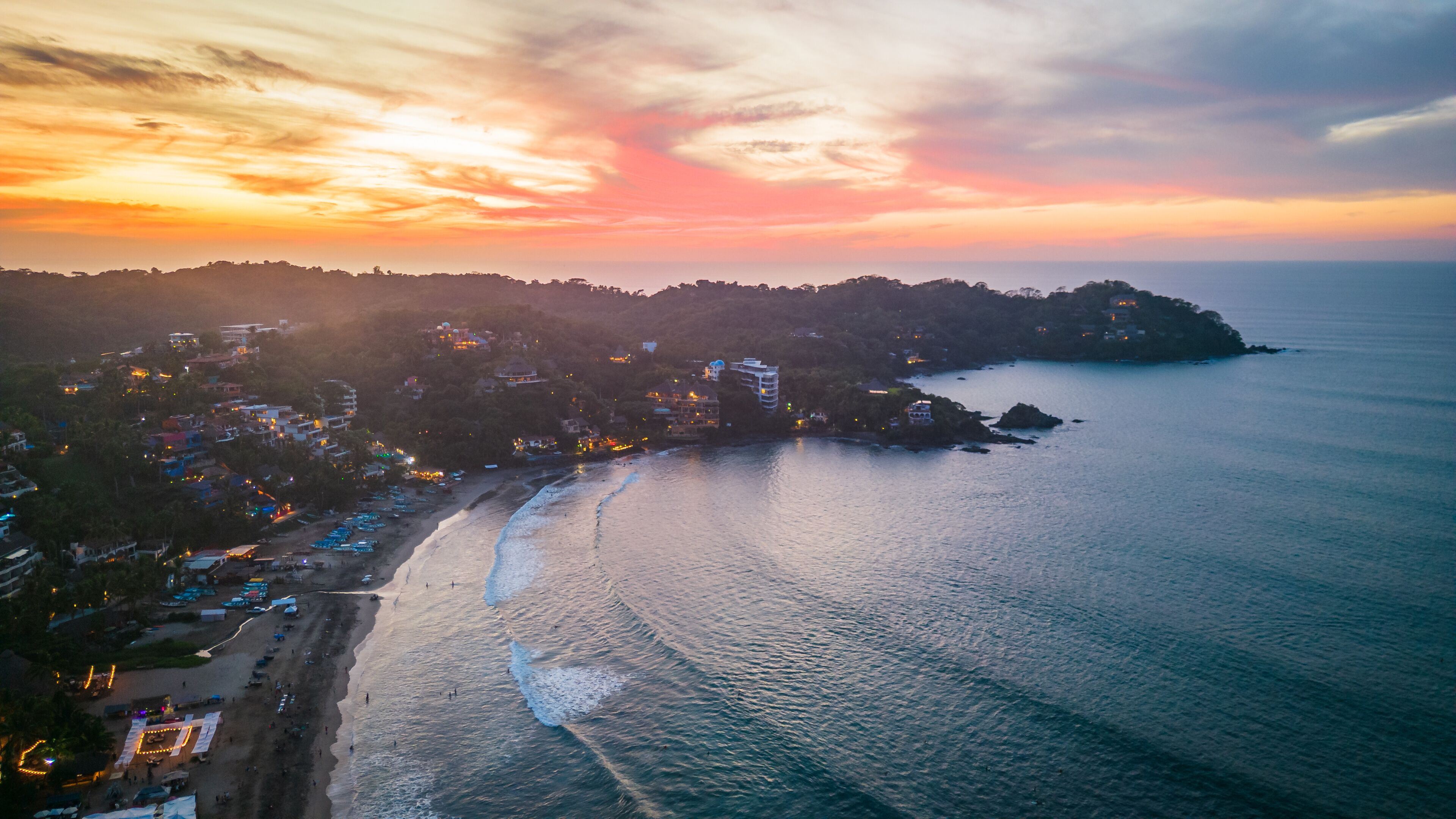 A coastal town with a beach, ocean, and a sunset sky.